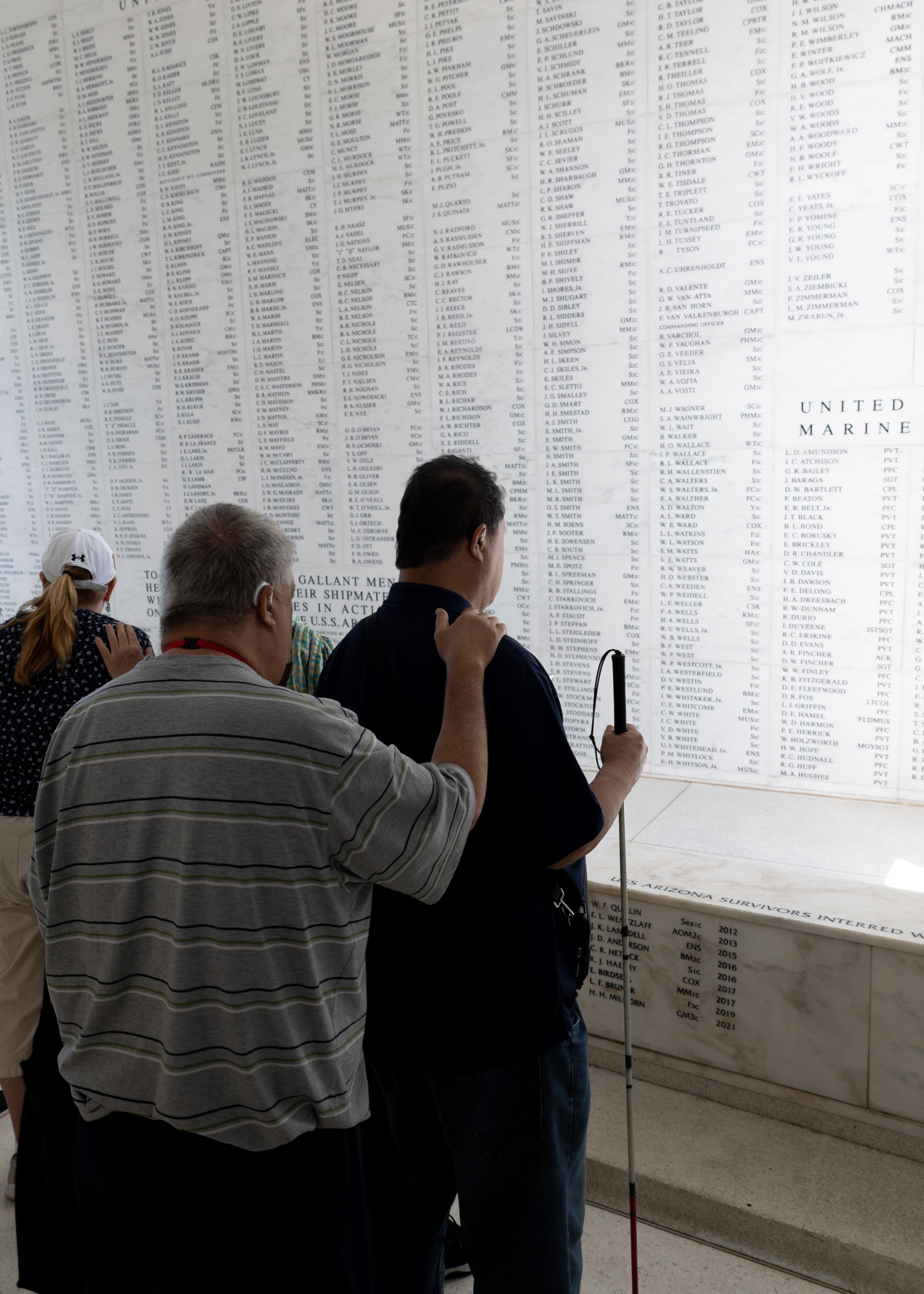 Hawaii Association of the Blind members Hilarion and Lance Kamaka stand silently and with reverance near the name-filled marble walls inside the U.S.S. Arizona Memorial. This Pearl Harbor National Memorial site commemorates the nearly 1,200 people who died on that ship when it was attacked and sunk on Dec. 7, 1941 in the Oahu harbor. Hilarion is standing behind his older brother and resting his right hand on Lance's right shoulder. Lance is holding a white cane, and the men also have visible hearing aids, indicating they are both hard of hearing and blind. The brothers recalled visiting the National Park Service site decades ago, as children, but had felt that the site at the time was inaccessible to them and not worthy of a return visit. That changed when they were invited back in April 2023 as part of a research project being conducted by The UniDescription Project. On this return visit, Lance said, the site's accessibility had improved greatly, and this improved access allowed him and his brother to properly pay their respects to the people who had perished and also to learn more about the history of the place and its role in World War II. For our part, the UniD research team has collaborated with the Hawaii Association of the Blind and the Pearl Harbor staff, including Chief of Interpretation David Kilton, to audio describe the site's official print brochures for Pearl Harbor National Memorial, the U.S.S. Arizona Memorial, the U.S.S. Oklahoma Memorial, and the U.S.S. Utah Memorial. Descriptions of those national park sites (and more than 200 others) are available now in the free UniD app (for iOS or Android).