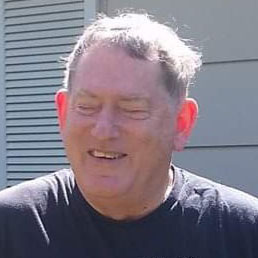 A middle-aged white male with peppered gray hair, which is shining in the sunlight. He is wearing a black t-shirt.