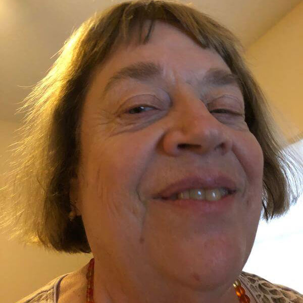 This is a headshot of a light-skinned Caucasian woman with brown highlighted hair and green eyes, who is smiling.